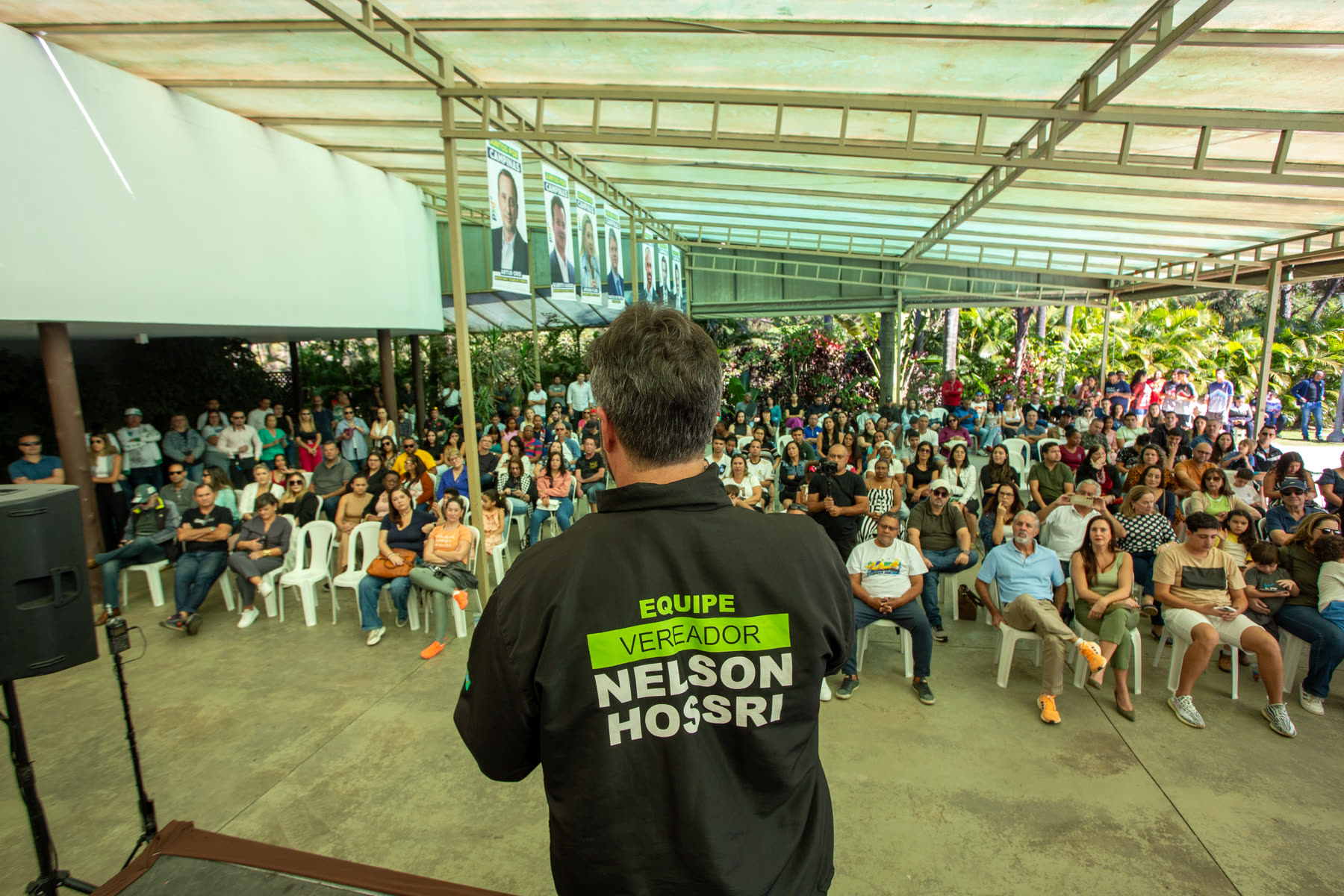 Nelson Hossri de costas, com a jaqueta da equipe, fala a um público sentado em um encontro de campanha em Campinas